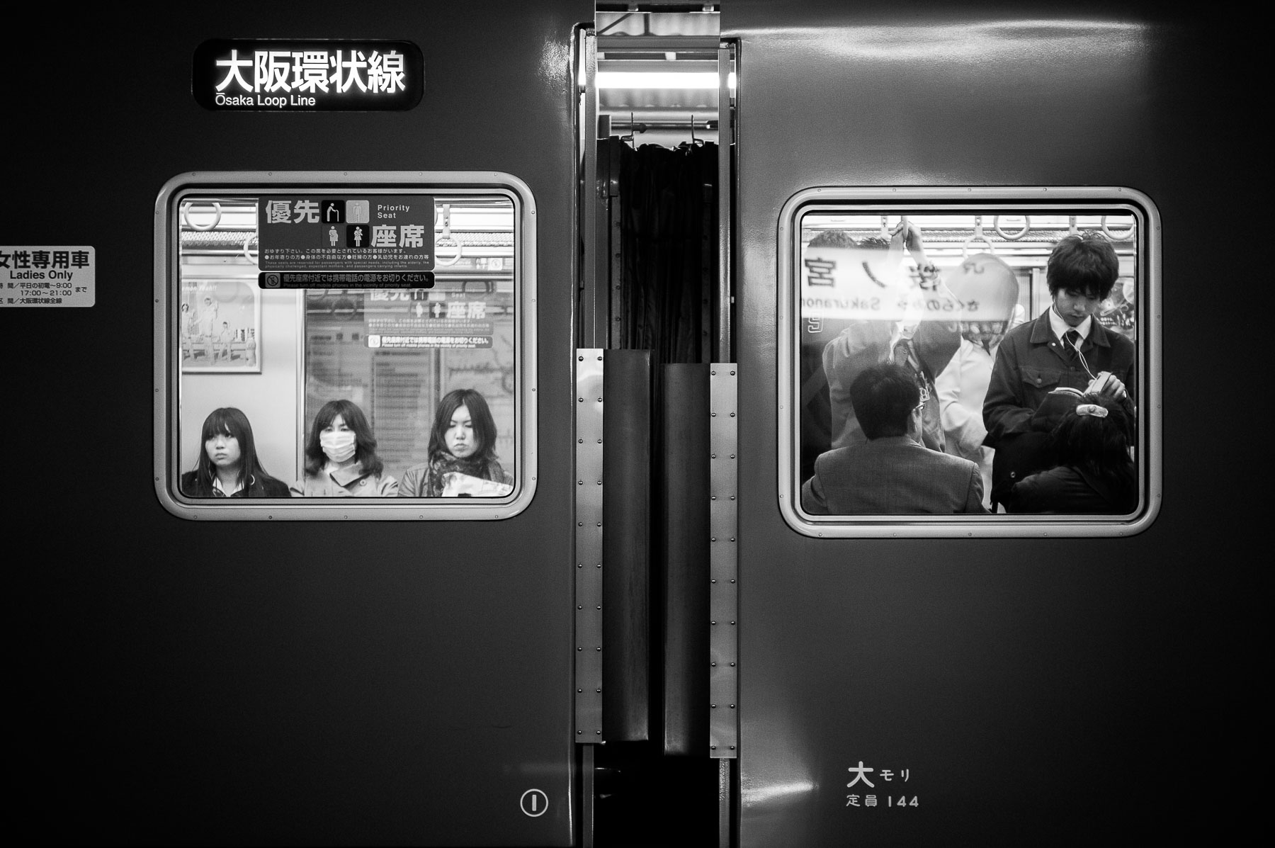 Black and white street photography of the Osaka subway, featuring two squared windows and people standing, showcasing the urban atmosphere of Japan